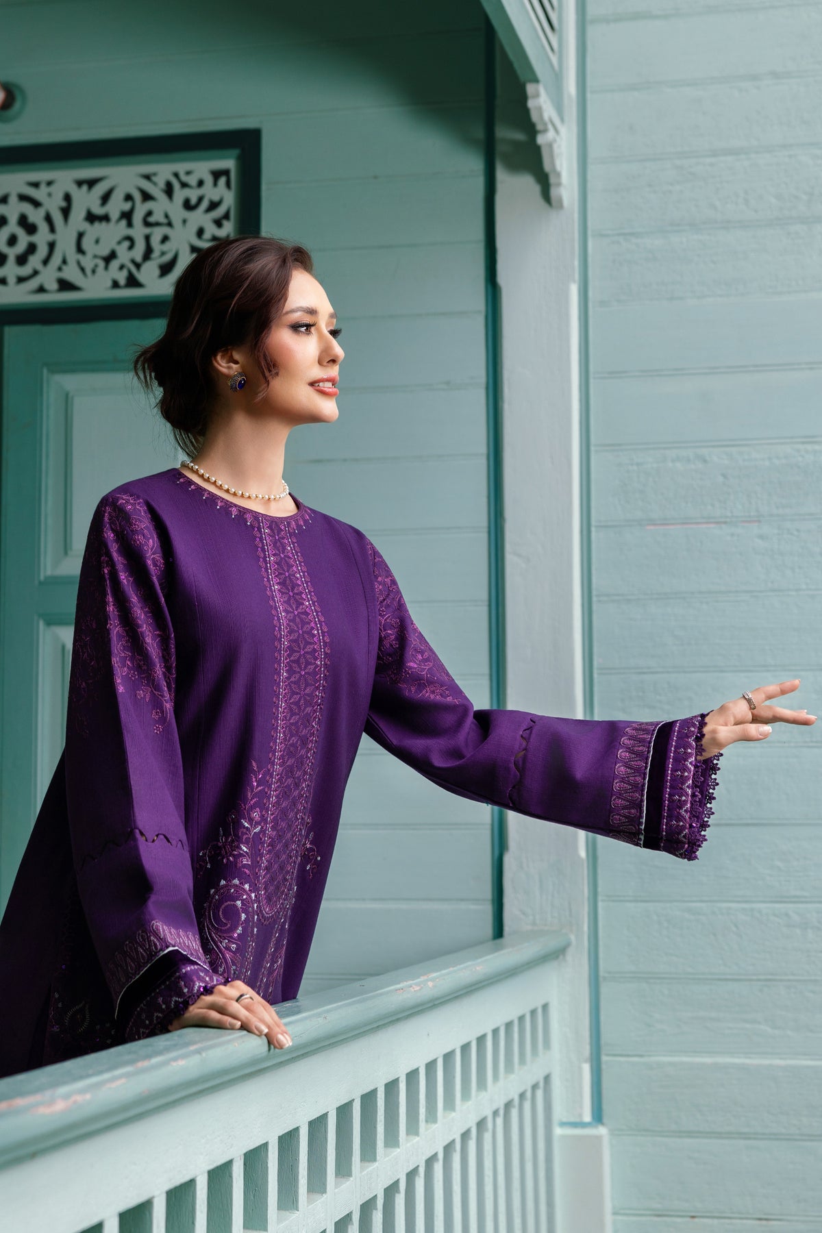 Woman in a purple traditional outfit standing on a balcony.